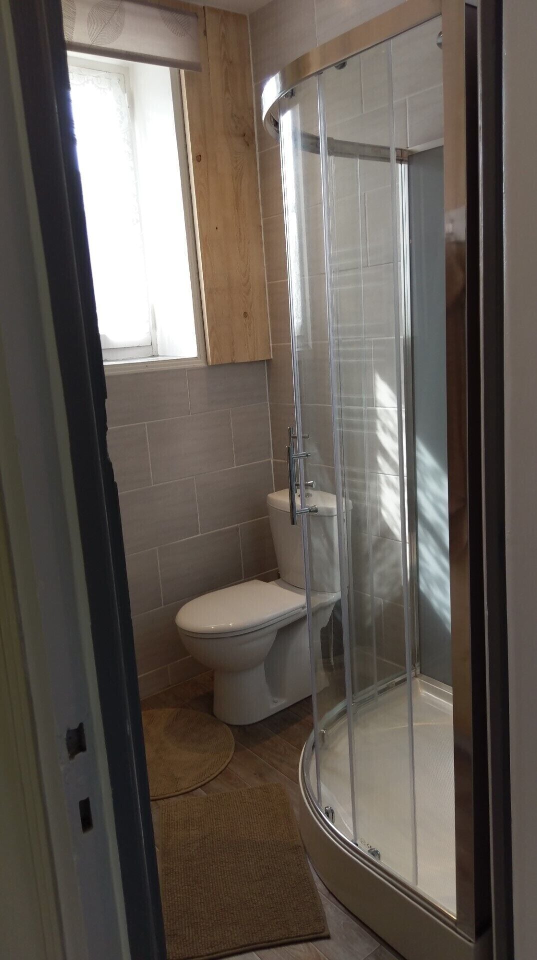 Een badkamer met een douchecabine, toilet en raam.