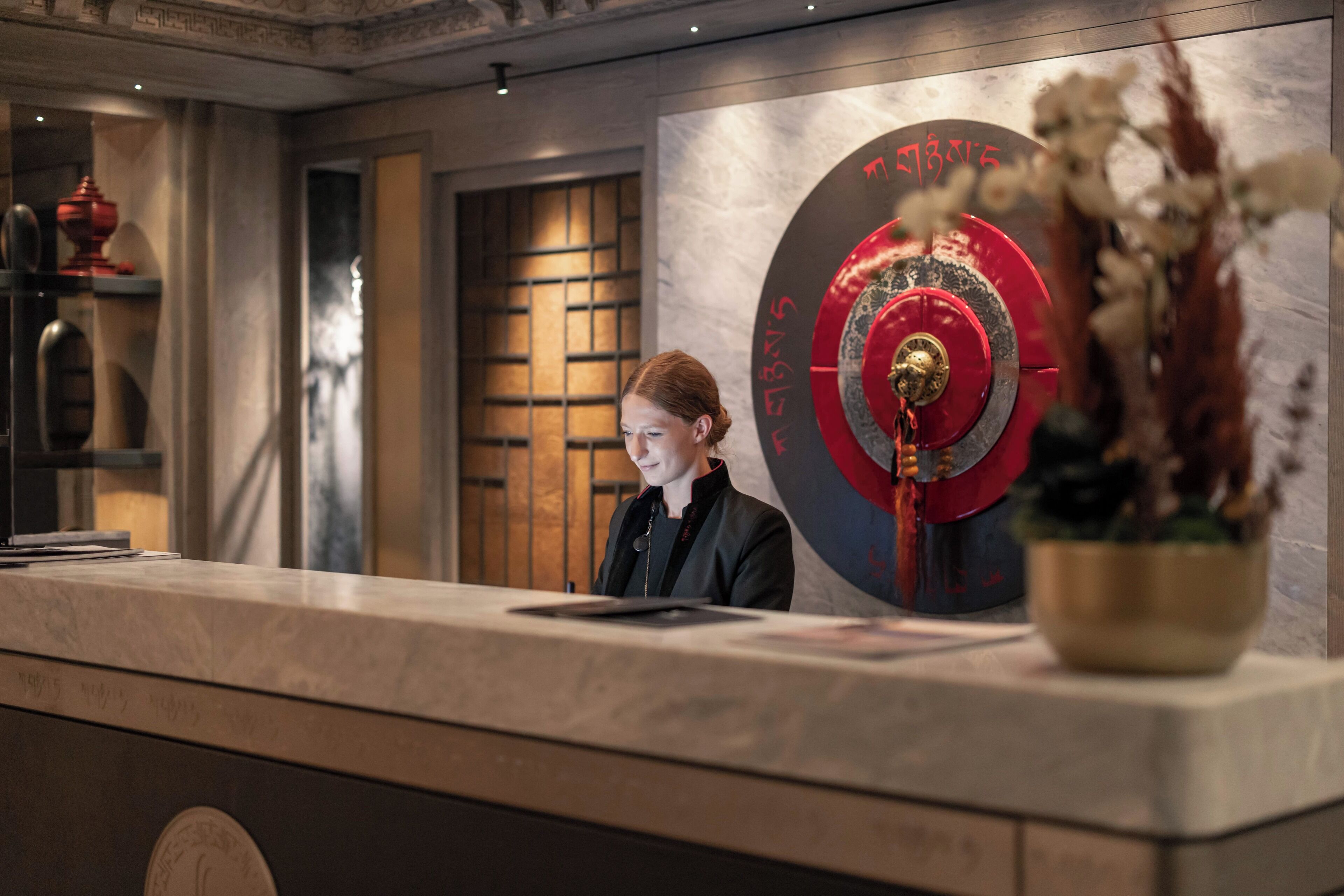 A reception desk with a large decorative clock and a vase of dried flowers.