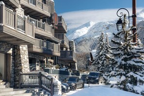 A multi-story building with stone and wood exterior, a balcony with a railing, and a snow-covered mountain in the background. - Hôtel le K2 Chogori (Val-d'Isere)