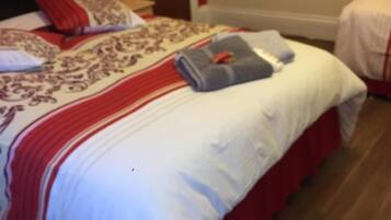 Una cama bien hecha con una colcha roja y blanca, una toalla doblada y una almohada.