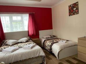 A bedroom with two beds, a window with red curtains, and a painting on the wall.