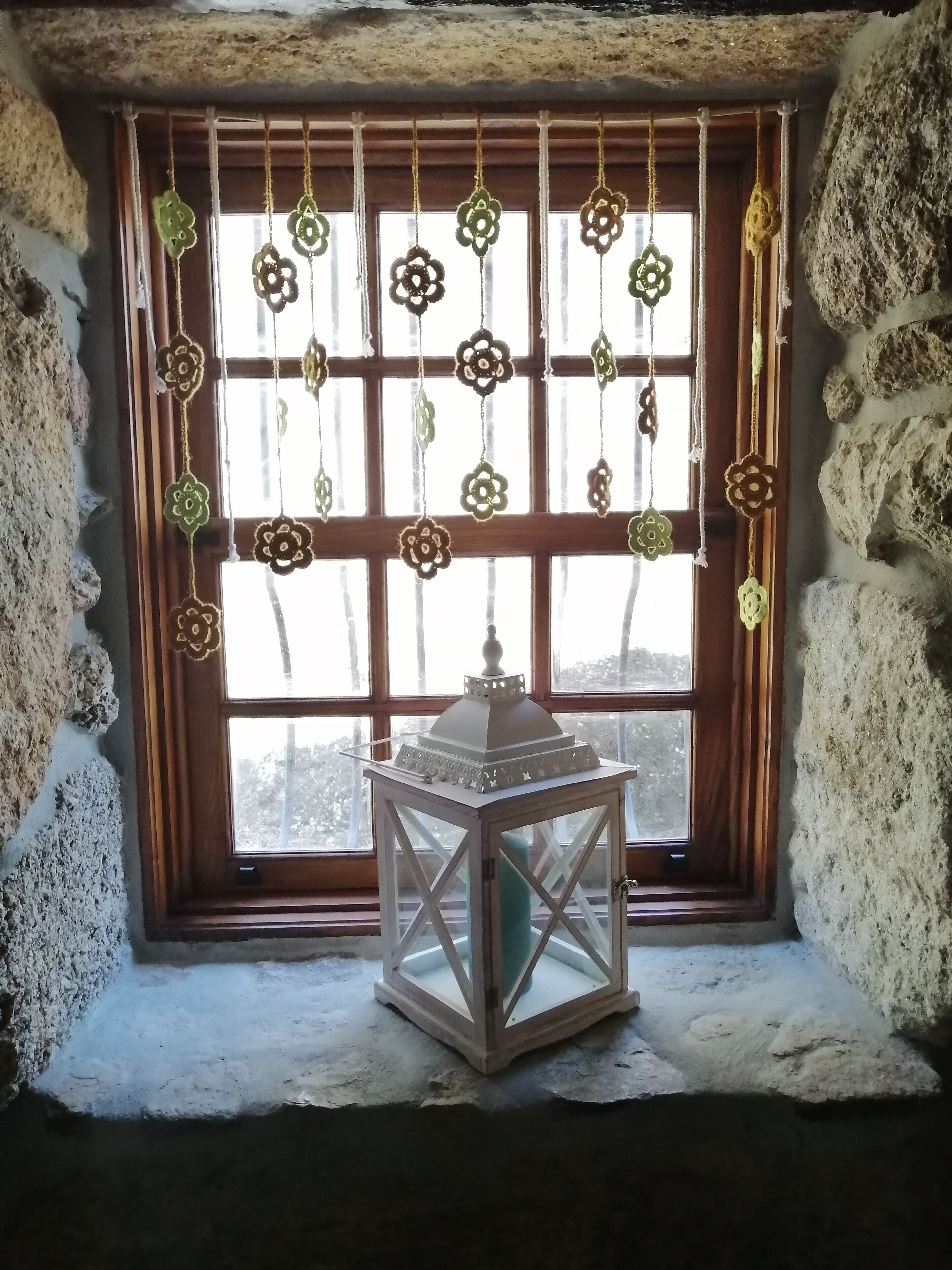 Une pièce avec un mur en pierre, une fenêtre en bois ornée d’une lanterne blanche et des décorations florales suspendues.