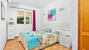 A bedroom with a bed, a nightstand, a dresser, a window with curtains, and a door. - VILLA AMALIA Family chalet. Private Pool, Free AC / Wi-fi (Cala en Porter)