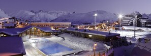 Un centro turístico cubierto de nieve con piscina climatizada, edificios de fachada de madera y un paisaje montañoso de fondo.