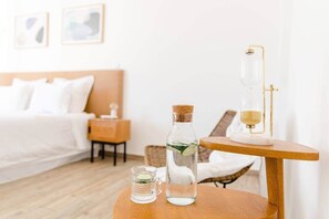 Ein Hotelzimmer mit Bett, Nachttisch, Tisch mit Wasserflasche, Glas Wasser und einer Kaffeemaschine.