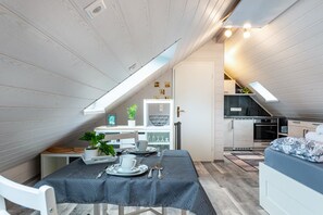 A compact, modern loft-style bedroom with a sloped ceiling, a built-in kitchen, and a dining area.