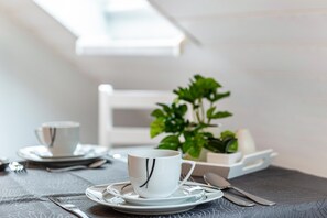 A dining table with a cup, saucer, and utensils, a small plant, and a white chair.