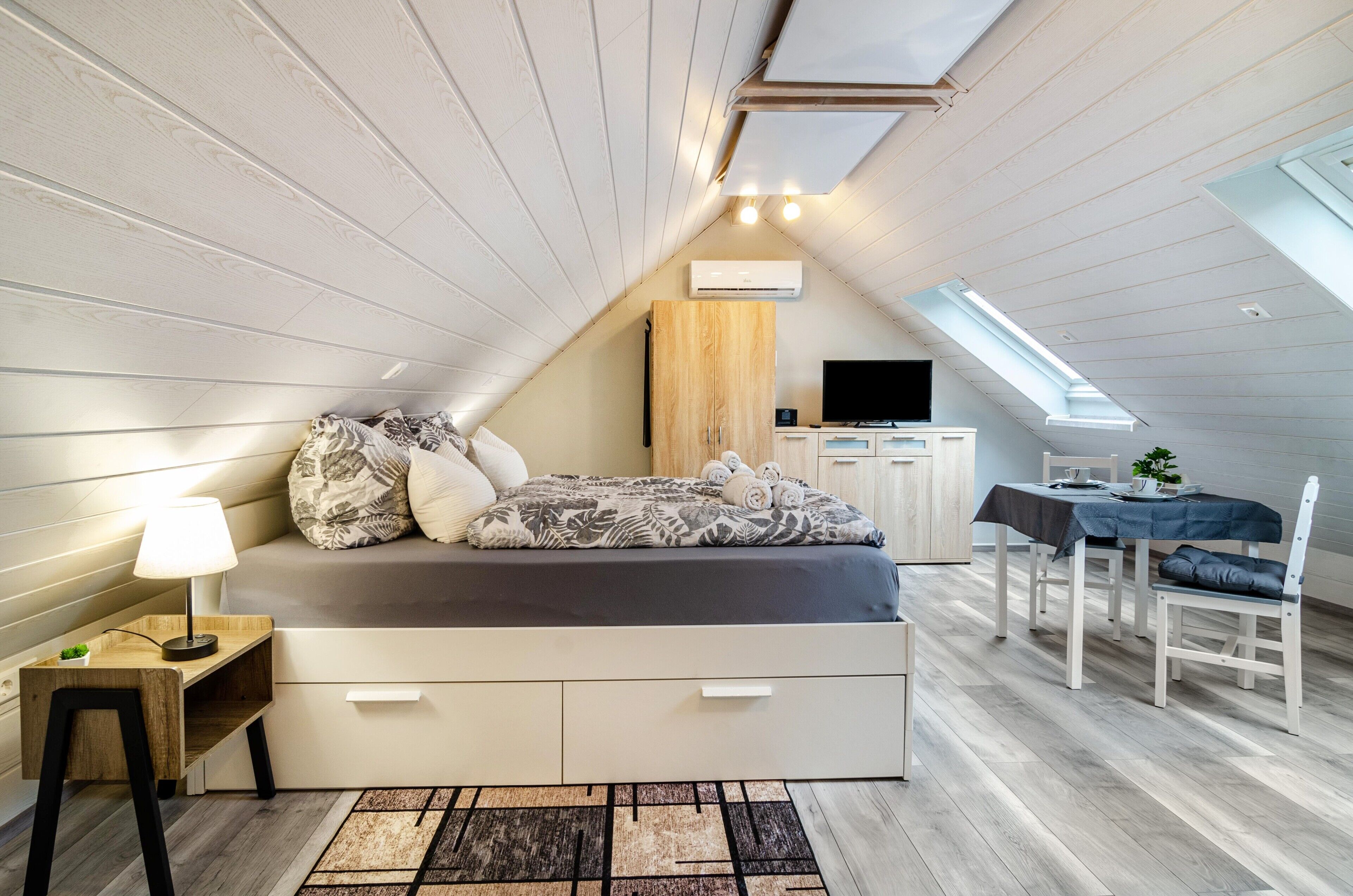 A bedroom with a bed, bedside table, lamp, and a desk with a chair.