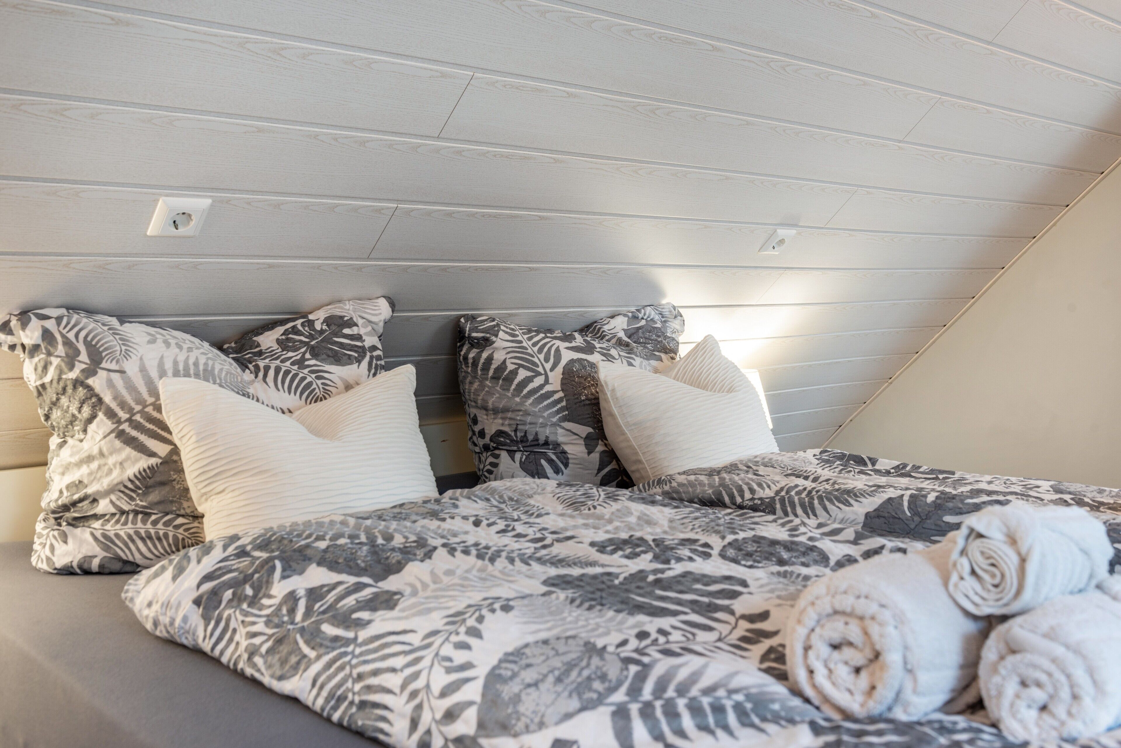 Une chambre avec un plafond en pente, un lit recouvert d’une literie à motifs floraux et des serviettes enroulées posées sur le lit.
