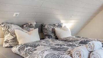 Une chambre avec un plafond en pente, un lit recouvert d’une literie à motifs floraux et des serviettes enroulées posées sur le lit.