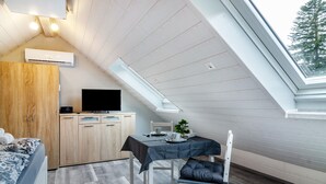 A room with a sloped ceiling, a dining table with chairs, a TV, and a wardrobe.