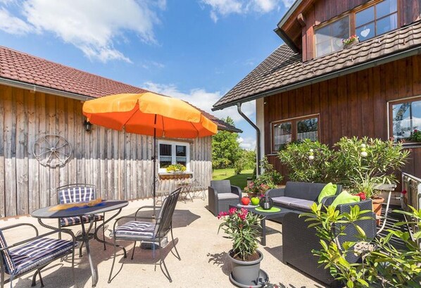 A wooden house with a patio area featuring outdoor furniture, a table, and an umbrella.