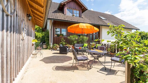 Una casa de madera con un patio amueblado, incluyendo mobiliario exterior y un paraguas grande color naranja.
