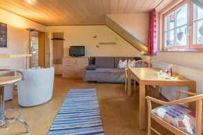A cozy room with a sofa, a TV, a dining table, and a staircase.