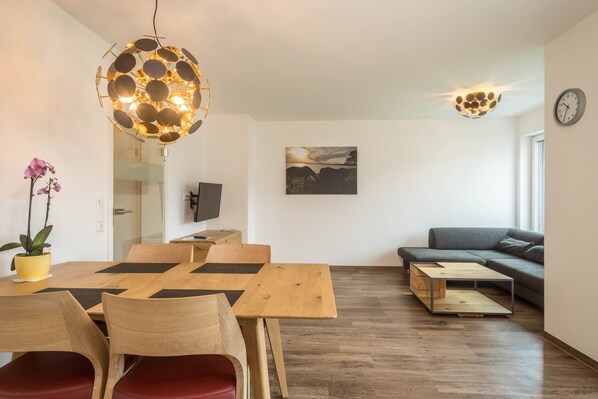 A modern living room with a wooden dining table, a sofa, a unique spherical light fixture, and a painting on the wall.