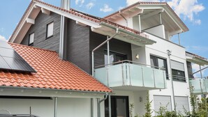Une maison moderne à deux étages, avec un toit recouvert de tuiles rouges, un balcon et une cheminée.