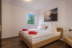 A bedroom with a wooden bed, white bedding, a window with a view, and a painting on the wall.