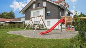 Une maison moderne dotée d’un espace de jeux pour enfants comprenant une balançoire et un toboggan.