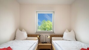 Une chambre avec deux lits, une fenêtre donnant sur la verdure et une table de chevet avec des lampes.