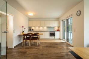 Una cocina moderna con armarios blancos, un comedor con sillas de madera y un ventanal grande.