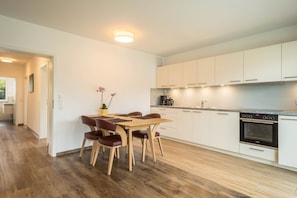 Una cocina moderna con armarios blancos, una mesa de comedor con sillas y un horno empotrado.