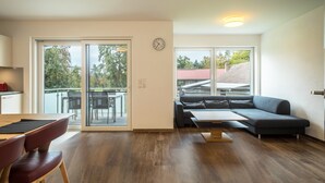 A modern living room with a sofa, a dining table with chairs, and a sliding glass door leading to an outdoor area.