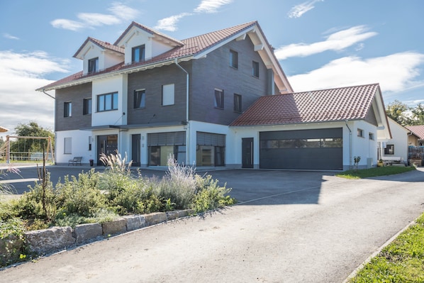 A two-story residential building with a garage, a driveway, and a landscaped front yard.