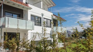 Una casa moderna de dos pisos con balcón, ventanas amplias y cielo despejado.