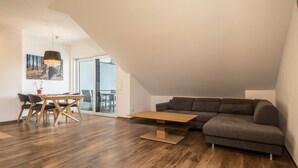 Una sala de estar moderna con una mesa de comedor de madera, un sofá gris y un ventanal grande.