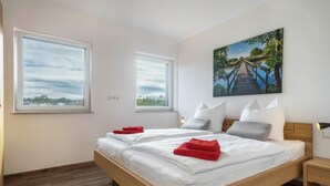 Ein Schlafzimmer mit einem hölzernen Bett, zwei Fenstern, einem Bild einer Brücke und einem Nachttisch.