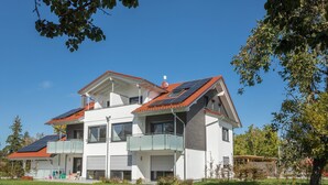 Ein modernes, zweistöckiges Haus mit Balkon, Solaranlage und rotem Dach.