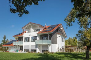 A modern two-story house with a balcony, solar panels, and a red roof.