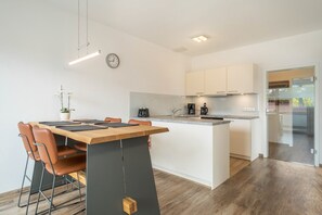 Una cocina moderna con una isla central, un comedor con sillas, un reloj y una planta en maceta.