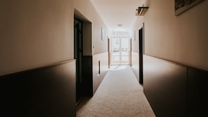 A hallway with a carpeted floor, a door at the end, and a light fixture on the ceiling. - Dworek Pani Walewska (Gdansk)