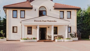 A two-story building with a white facade and a red-tiled roof. The name "Dworrek Pani Walewska" is displayed above the entrance. There are potted plants and outdoor furniture in front of the building. - Dworek Pani Walewska (Gdansk)