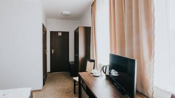 A hotel room with a bed, a desk with a television, a chair, and a door with a 'no entry' sign.