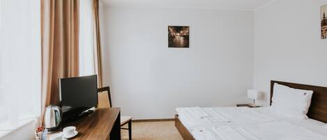 A hotel room with a bed, a desk with a TV, a coffee maker, and a small table with cups.