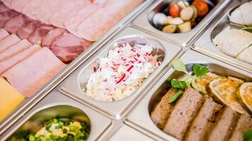 A buffet with various food items including sliced meats, a salad with shredded vegetables, and a dish with sliced bread.