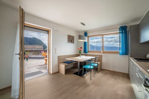 Et moderne køkken med spiseplads, et stort vindue med udsigt til naturen, og en skydedør til et udendørs siddeområde.