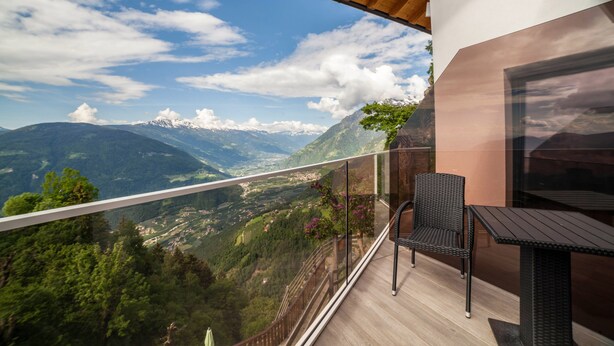 A balcony with a view of mountains, a table, and a chair.