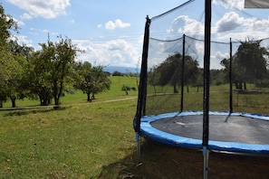 Un trampoline installé dans un espace extérieur verdoyant, avec des arbres et un ciel dégagé.