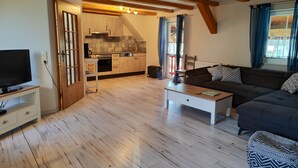 Sala de estar com sofá, mesa de centro, TV e cozinha ao fundo.