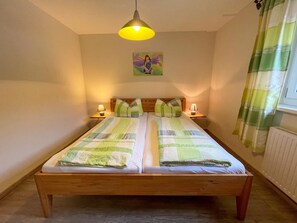 A double bed with a wooden frame, two bedside tables with lamps, a painting on the wall, and a window with curtains.