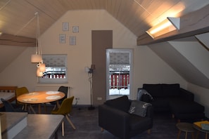 A room with a dining table, chairs, a sofa, and a window with blinds.