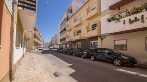 En smal stadsgata kantad av höga byggnader, parkerade bilar och en klar himmel.