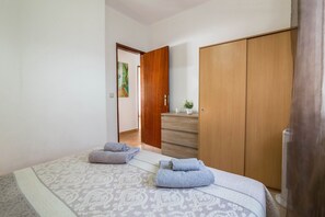 A bedroom with a bed, a wooden wardrobe, a dresser, and a fan.