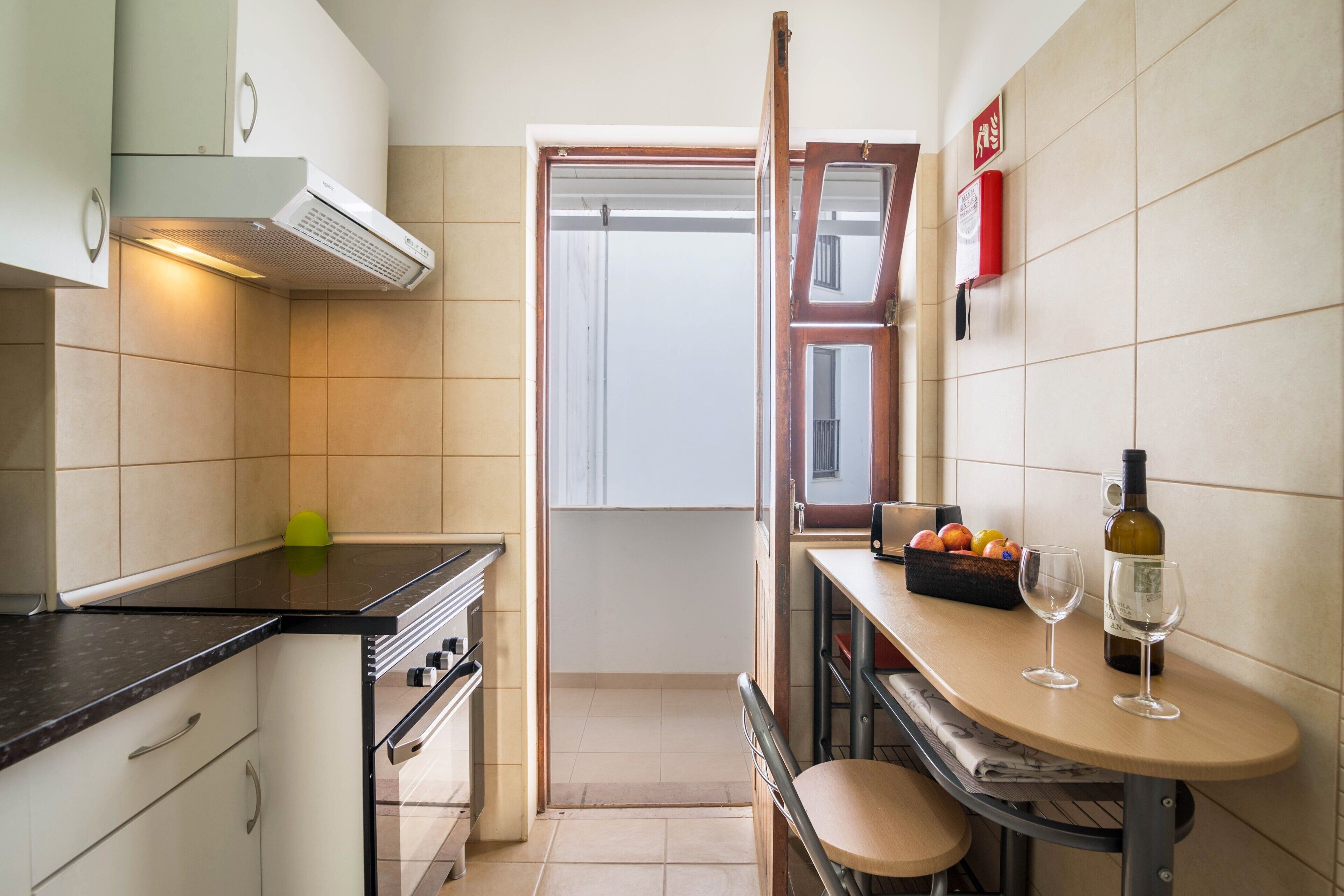 Une cuisine compacte équipée d’une cuisinière, d’un four et d’un petit coin repas avec une table et deux verres à vin.