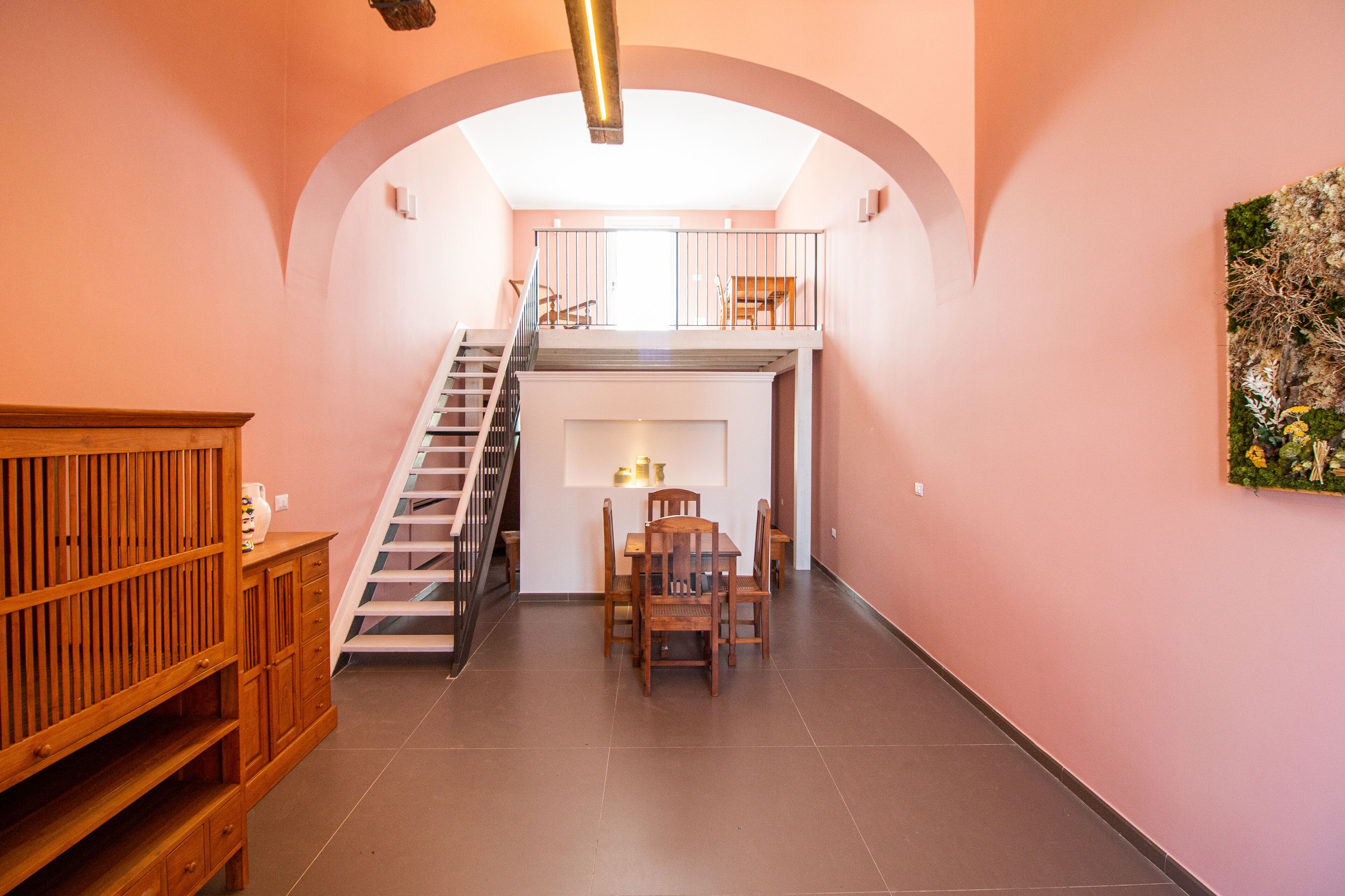 A spacious interior with a staircase leading to an upper level, a dining area with a table and chairs, and a wooden cabinet.