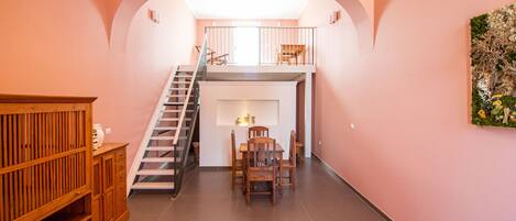 A spacious interior with a staircase leading to an upper level, a dining area with a table and chairs, and a wooden cabinet.