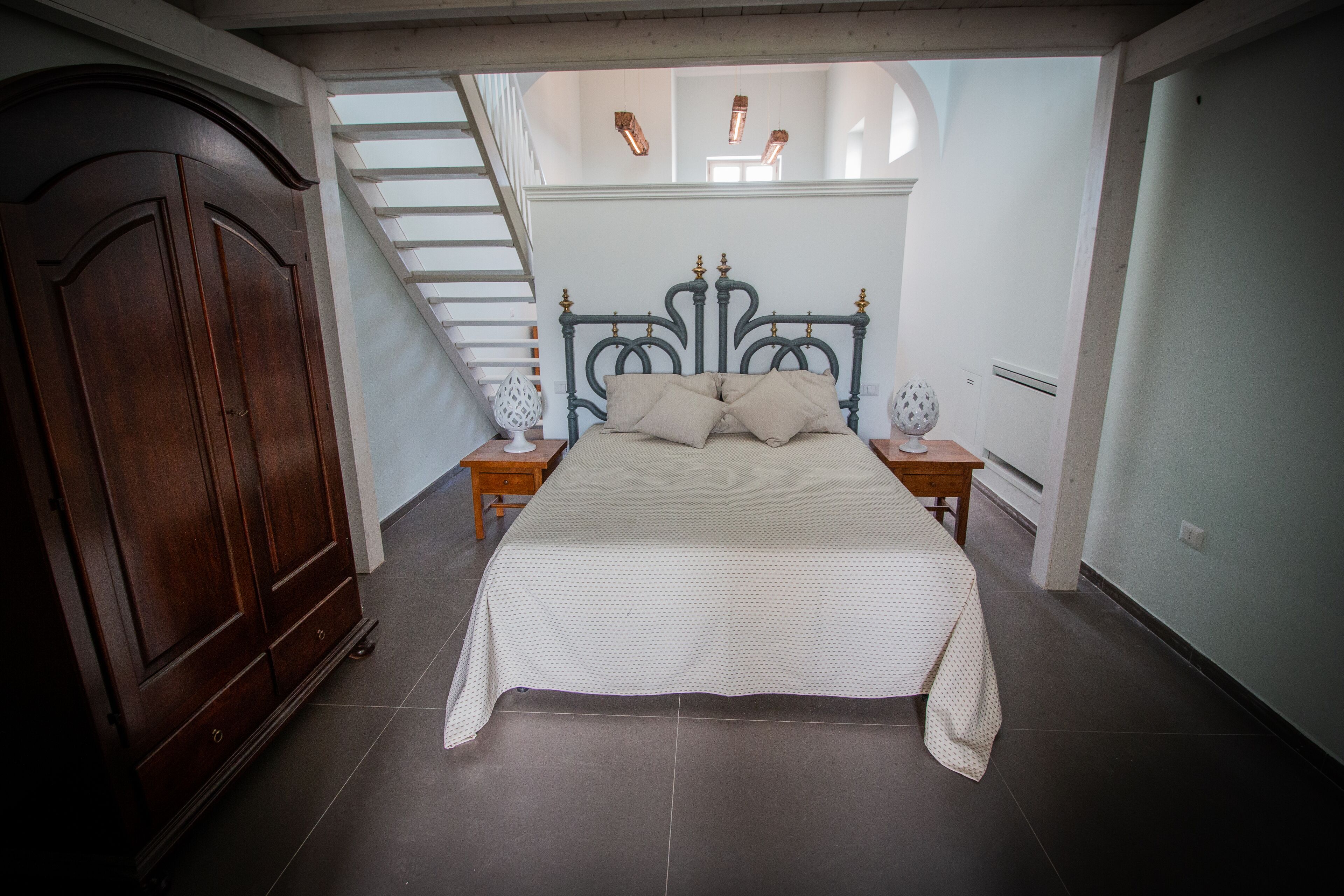 A bedroom with a bed, nightstands, a wardrobe, and a staircase leading to an upper level.